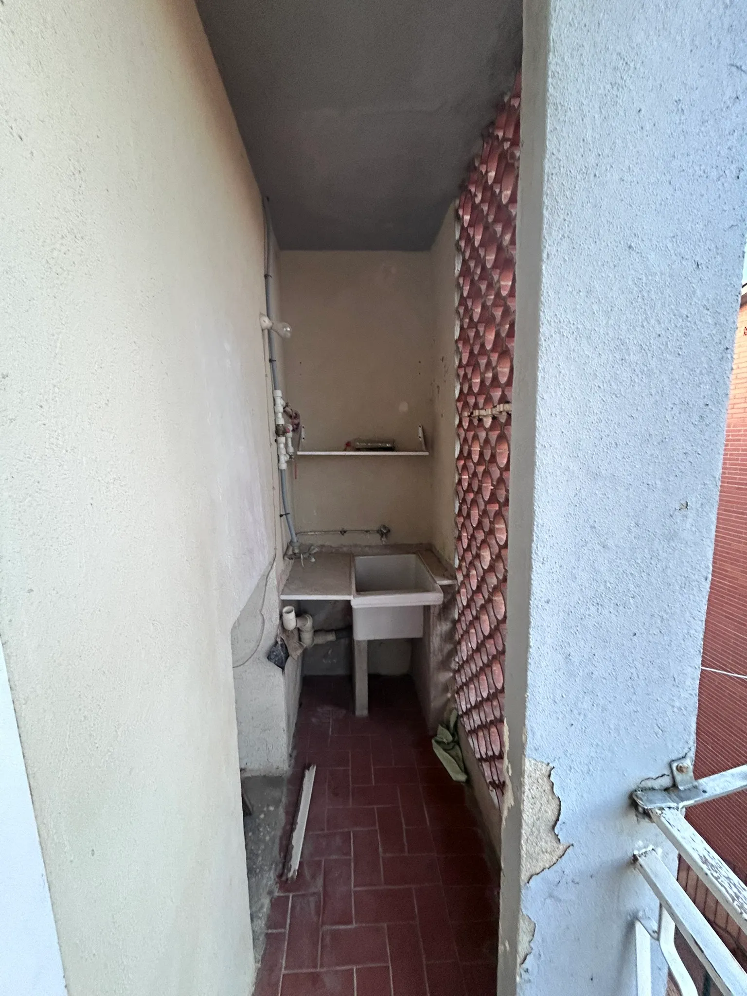 Galería estrecha original con pila de obra, tuberías vistas por la pared, suelo de gres rojo y celosía de ladrillo