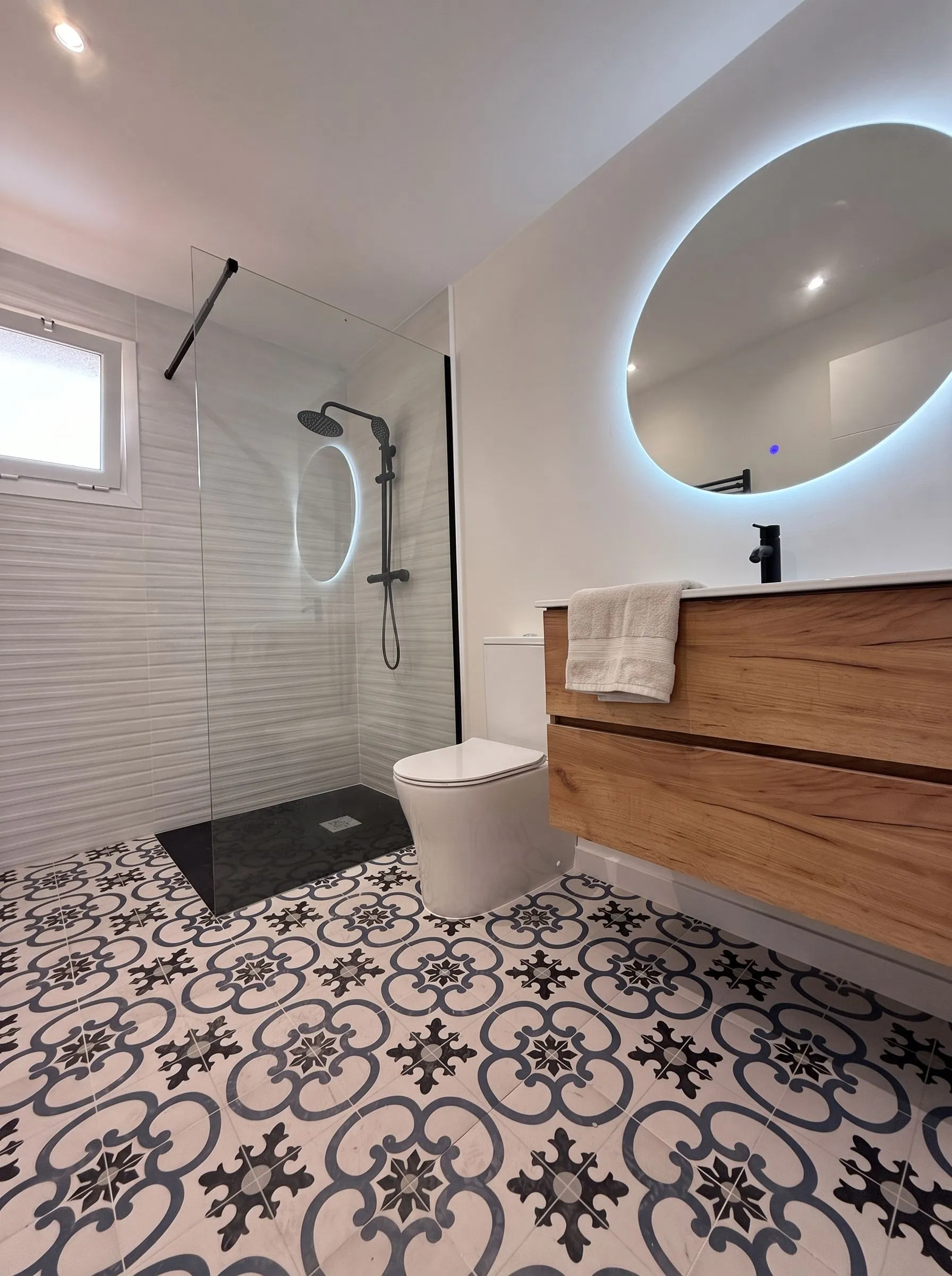 Baño principal reformado en Girona, Carrer Astúries: espejo retroiluminado, mueble de roble y suelo hidráulico.