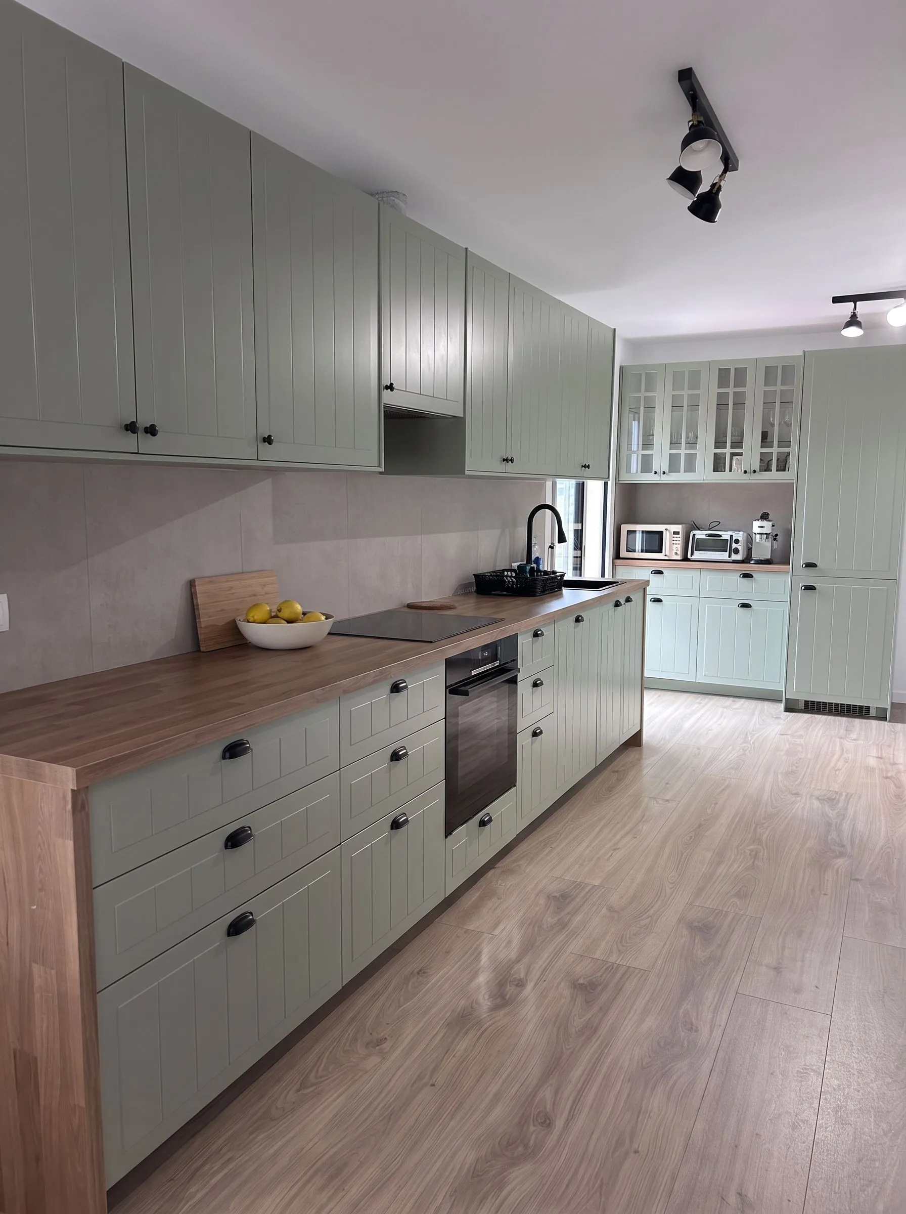 Cocina reformada en Banyoles: frentes verde salvia, encimera de madera y tarima, ya en uso por la familia.